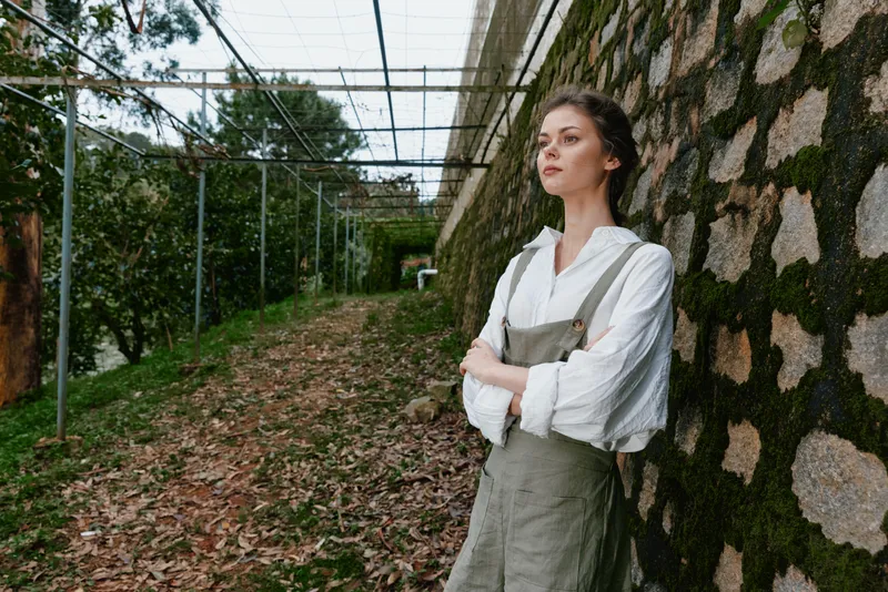 Young woman in a stylish outfit with a serene expression, posing against a rustic stone wall in a natural setting, emphasizing a connection to nature and eco friendly fashion