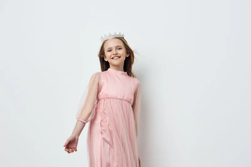 Smiling girl in a pink dress posing joyfully against a white background, embodying innocence and playfulness, ideal for concepts like childhood and fashion