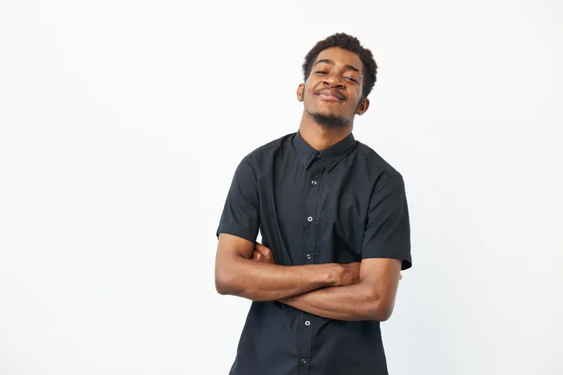 Confident black man smiling with arms crossed, showcasing a relaxed and positive attitude against a minimalist white background.