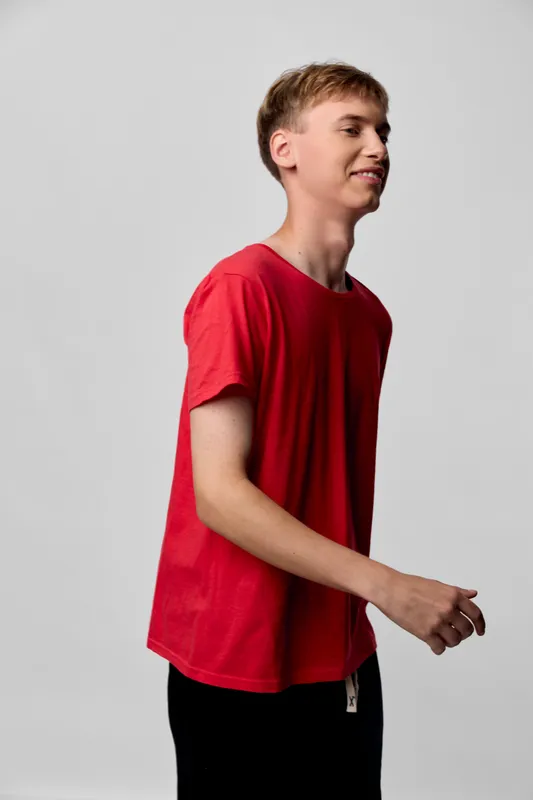 Teenager in a red t shirt walks past the camera in a studio, displaying casual wear, movement, and confident demeanor that captures youth energy and everyday style in a simple composition.
