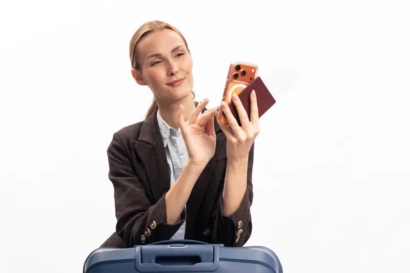 Young woman holding passport and smartphone with luggage on white background. Concept of travel planning, vacation preparation, and booking tickets. Casual outfit and happy expression.