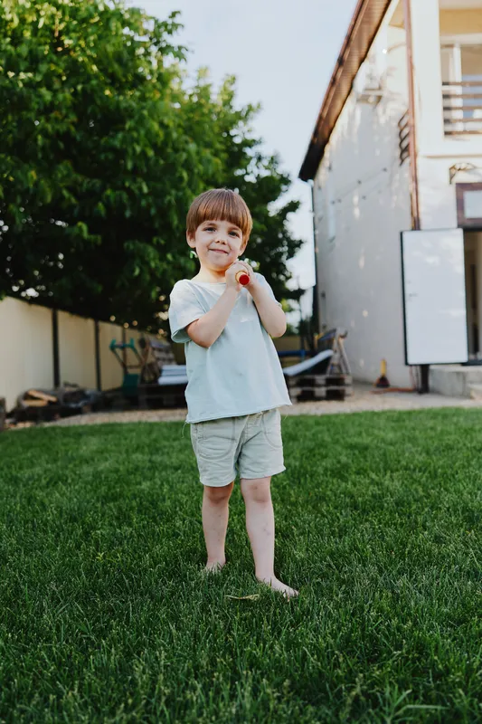 Happy boy playing outdoors in a sunny backyard, enjoying family time with a toy. His laughter adds joy to the warm summer day in a vibrant setting.