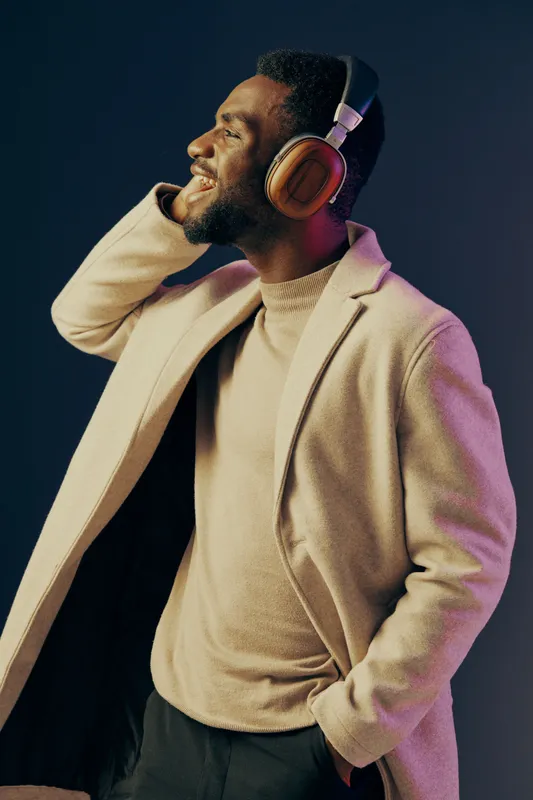 Young Black man enjoying music with headphones in stylish coat, smiling against a colorful background, conveying joy and relaxation