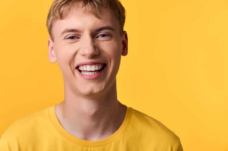 Smiling man in a bright yellow shirt against a vivid yellow background, exuding happiness and energy, casual style with a friendly expression suitable for lifestyle and fashion branding