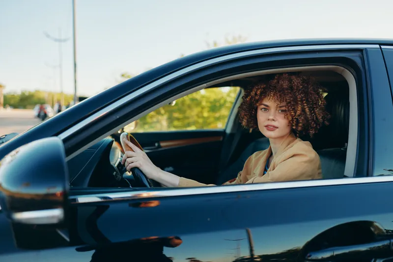 A woman driver sits in a car with daylight flooding the cabin, capturing a casual lifestyle moment in retro film color and warm nostalgic tones.