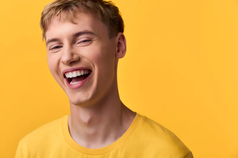 Smiling man in a yellow shirt against a bright yellow background, conveying happiness, energy and warmth in a close up lifestyle shot