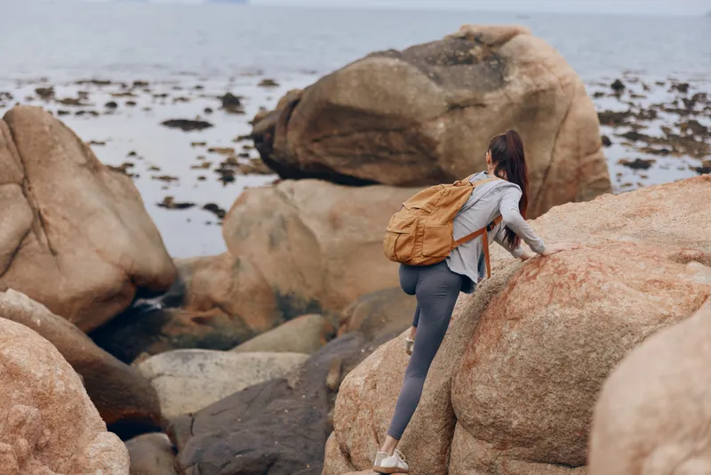 Young woman climbing rocks by the sea with a backpack, illustrating adventure and exploration in a natural setting Outdoor activity emphasizing nature s beauty