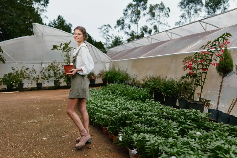 Young woman caring for plants in a greenhouse, highlighting sustainability, nature, and healthy living in a serene green environment