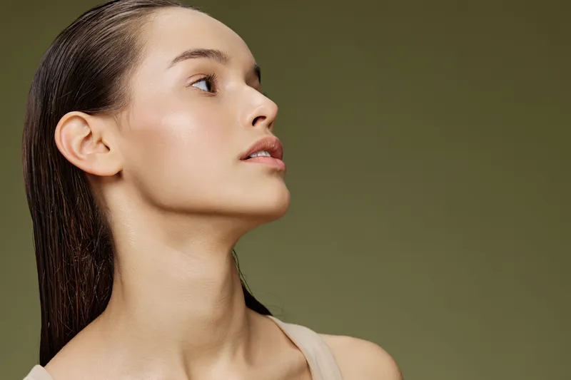 Elegant portrait of a woman with wet hair showcasing a natural look, highlighting beauty and skin texture against a muted green background