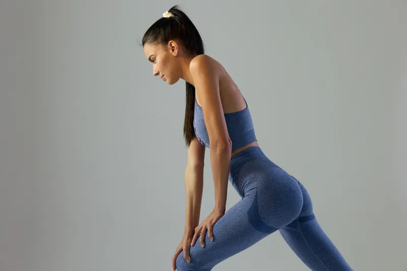 woman sport fitness stretching in blue workout clothes focused and strong with ponytail on neutral background, active lifestyle and health concept