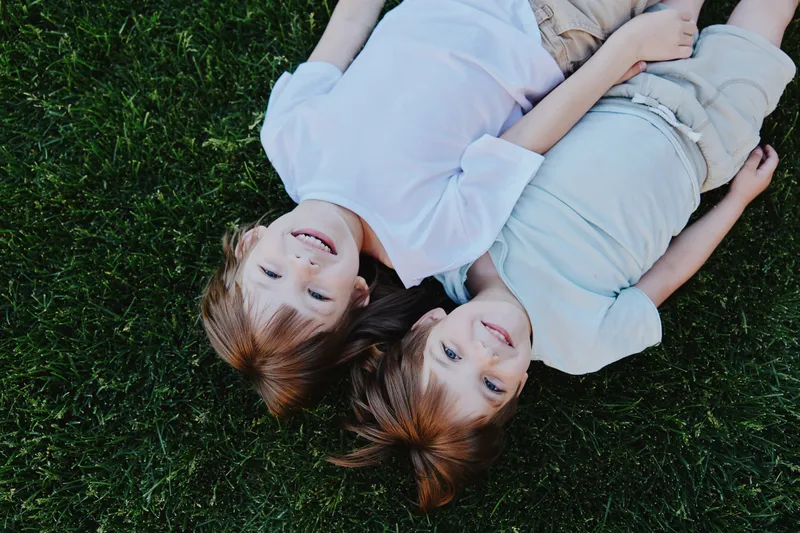 Happy children lying on the grass, enjoying a sunny day, laughing together, carefree moments, friendship, summer joy.