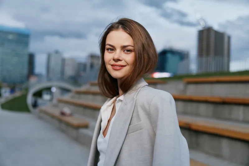 confident woman in light gray blazer smiling outdoors with urban cityscape background in spring season business concept