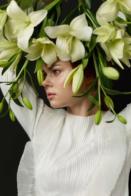 A serene young woman with an elegant white outfit adorned with fresh lilies, symbolizing beauty and nature, showcasing a modern, organic lifestyle