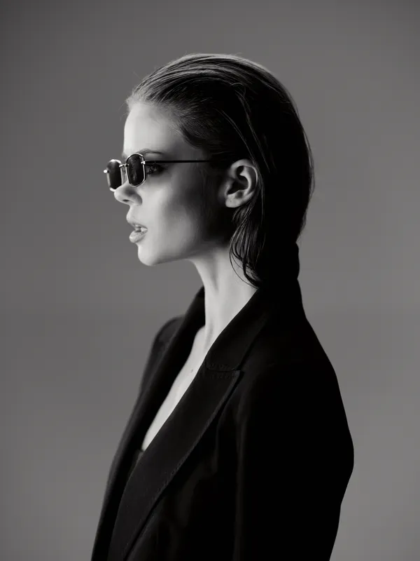 Black and white portrait of a stylish woman wearing sunglasses and a dark coat, showcasing modern fashion and elegance.