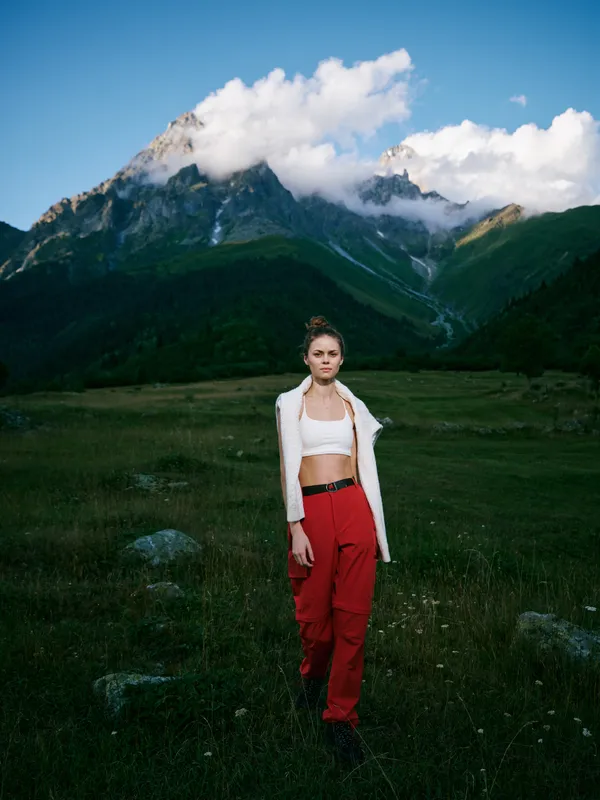 Mountains, meadow, woman, outdoor fashion travel landscape nature adventure scenery in alpine valley with clouds and grass under a clear sky, stylish casual look and wild landscape mix