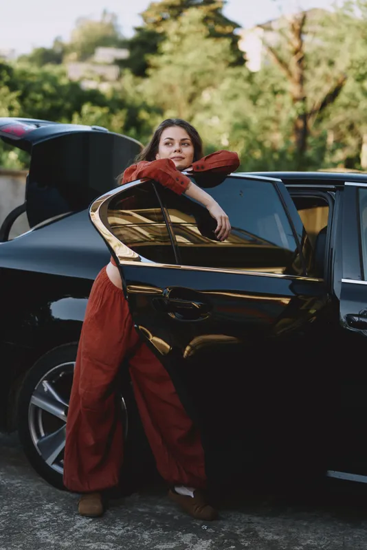 A young woman leans out of a parked car door, relaxed and curious, posing in a casual street scene that captures authentic everyday lifestyle and candid city vibe