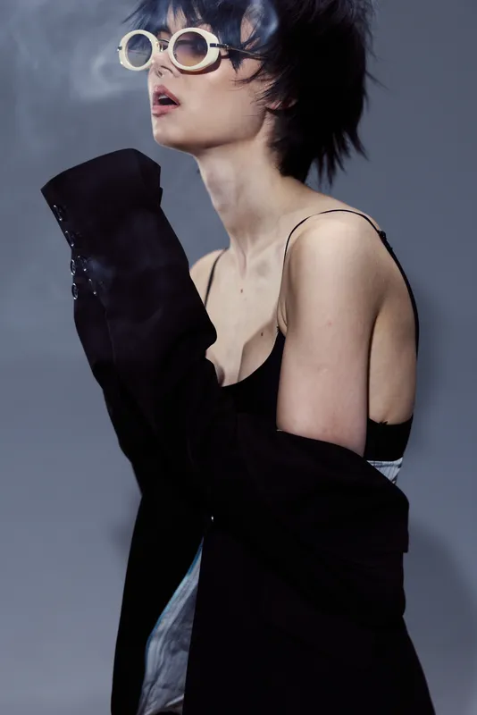 Stylish woman with short hair wearing sunglasses and black clothing in moody lighting and smoky background