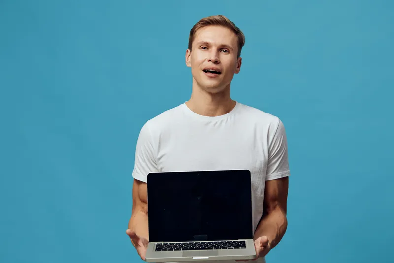 smiling young caucasian man hold laptop show screen wear white t-shirt isolated on blue background digital nomad concept