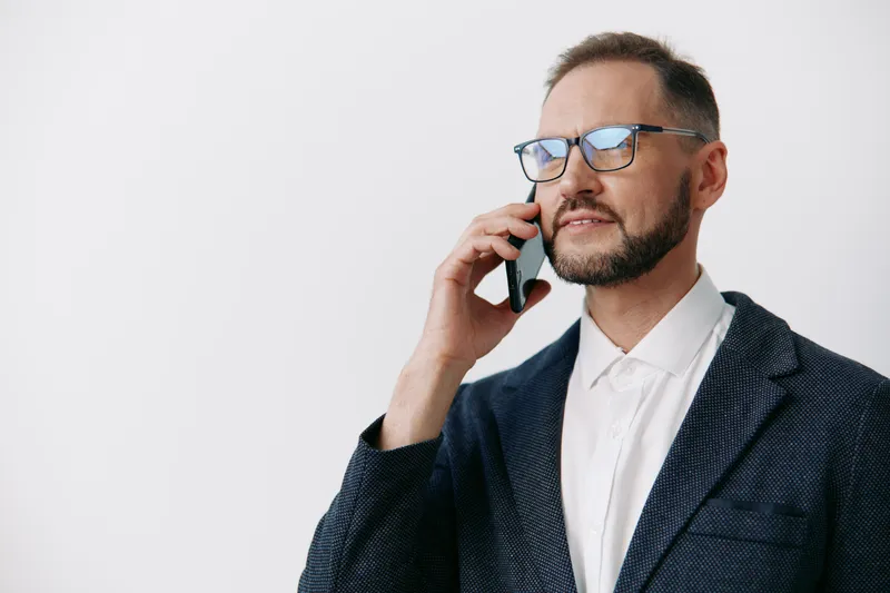 Professional man in a suit speaks on a mobile phone against an isolated white background, clearly conveying confidence, focus, and strong executive presence for business imagery.