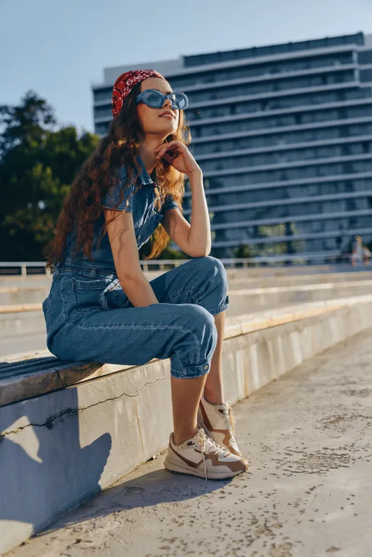 Lifestyle woman wearing modern boho-western denim street style outfit sitting outdoors in warm sunlight with film color effect and casual relaxed expression.