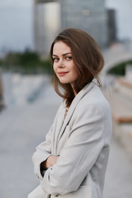 Confident businesswoman in a grey blazer smiling confidently against a modern urban background, embodying professionalism and ambition in her career.