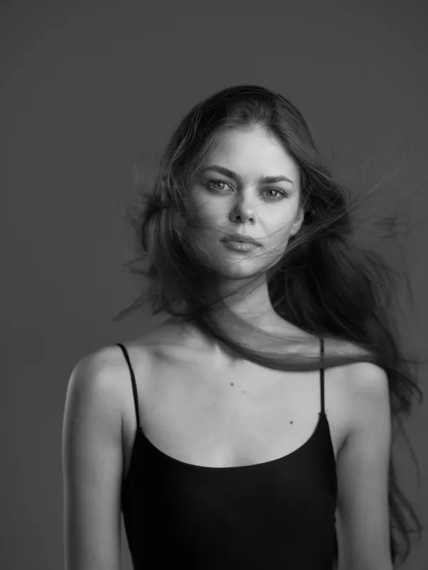 Black and white portrait of a young woman with loose hair wearing a black sleeveless top looking calm and confident