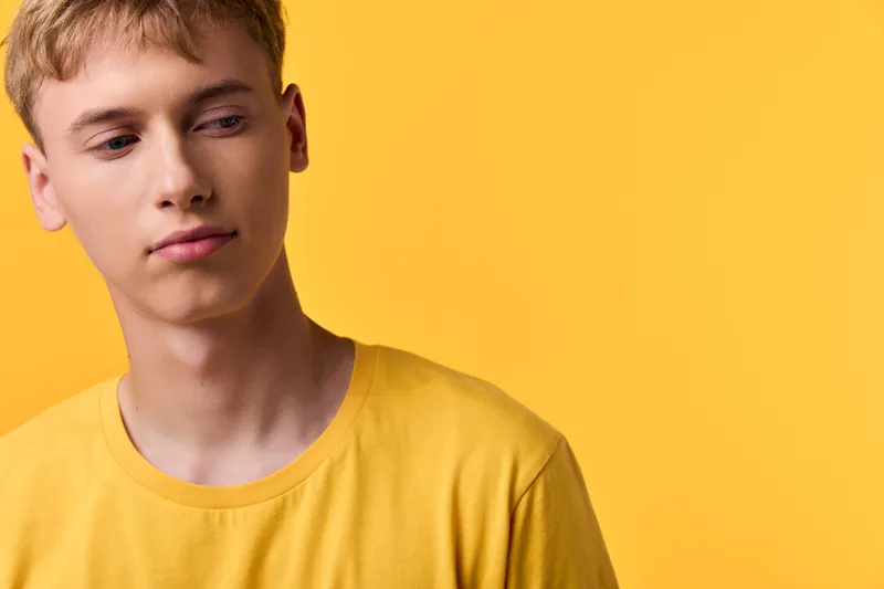 Yellow man in casual shirt in a studio with a focused expression against a bold color background, creating a clean fashion mood and simple composition