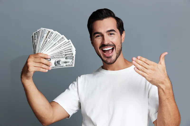 Excited smiling man holding banknotes in hand, celebrating financial success with joy. Isolated on a solid gray background portrait style.