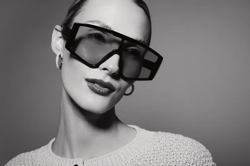 Young Caucasian woman with fair skin wearing oversized sunglasses and hoop earrings in black and white portrait. Fashion concept.