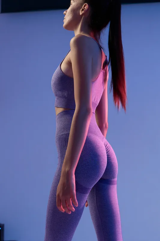 Sport fitness woman standing sideways in tight activewear, toned body, focused expression, illuminated by blue and purple soft lighting, modern athletic style.