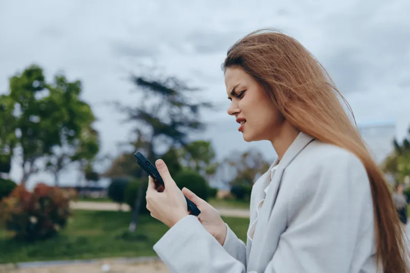 Professional woman using smartphone outdoors with a serious expression in a modern urban environment.