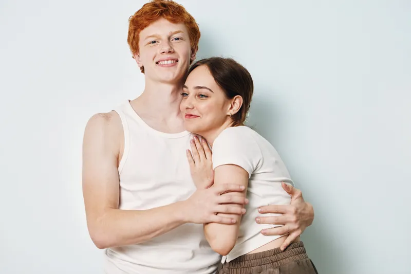 Young couple hugging and smiling together with white background. Man and woman in casual clothing embracing for love, friendship and happiness in studio portrait.