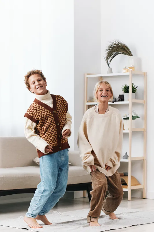 Two joyful adults dancing in a bright living room, wearing cozy sweaters and relaxed jeans, capturing carefree movement, bright smiles, and a warm casual fashion moment.
