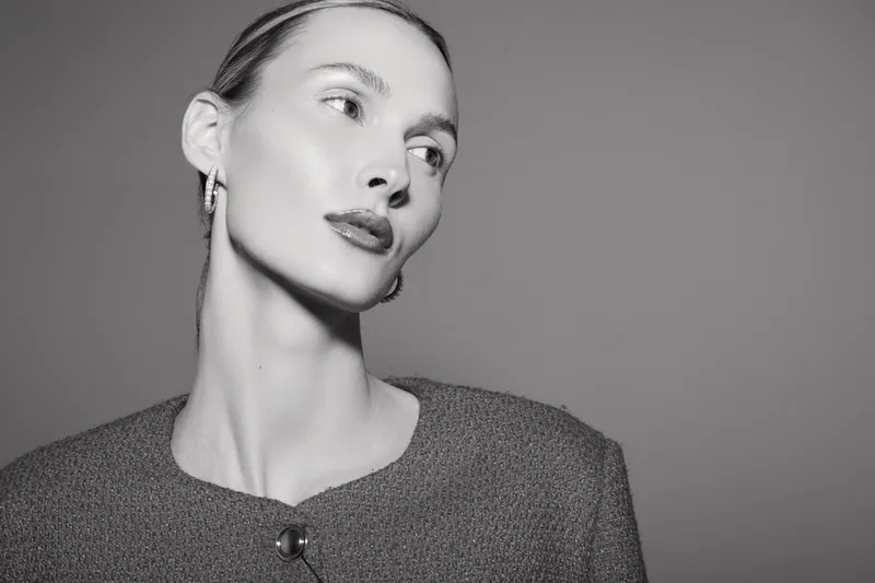 Portrait of a young white woman with pale skin wearing a textured jacket and earrings looks aside with soft lighting on grey background. Concept of elegance and fashion.