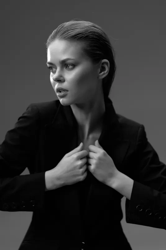 Black and white portrait of a serious young woman in a suit looking away with dramatic lighting and a neutral background