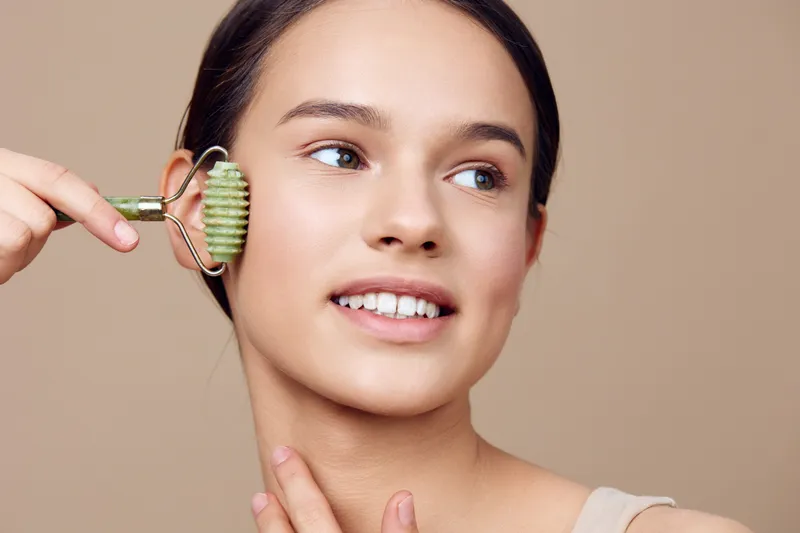 Young woman enjoying facial massage with a jade roller, promoting skincare and wellness, featuring a soft neutral background and natural glow
