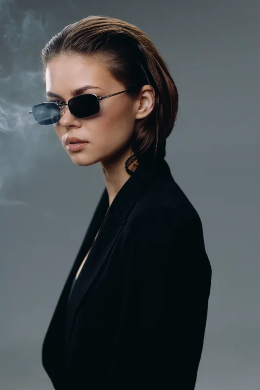 Stylish woman wearing sunglasses in black outfit with smoky background and serious expression