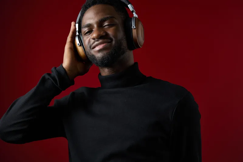 Smiling Black man in headphones enjoying music against a deep red background, showcasing a modern and stylish vibe for music lovers