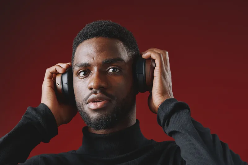 Young Black male wearing headphones, expressing surprise against a deep red background, suitable for music, technology, and lifestyle themes