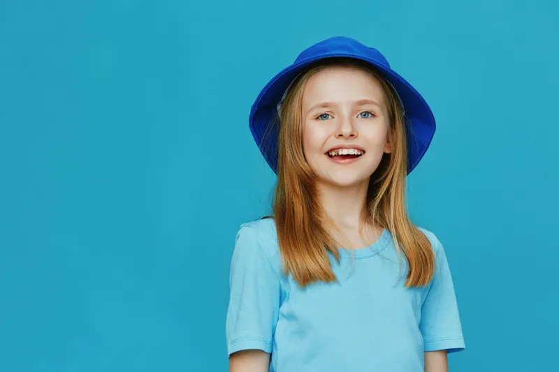 Happy girl wearing a blue hat and a blue shirt, smiling against a vibrant blue background, perfect for youth fashion and summer themes
