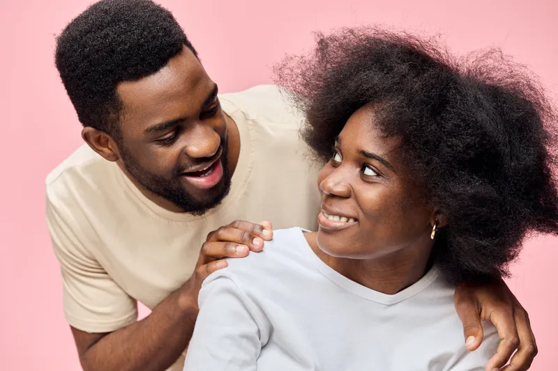 Happy African couple with natural hairstyles sharing a joyful moment against a pink background, showcasing love and connection in a modern setting