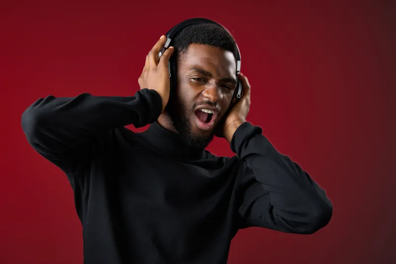 Excited young black man enjoying music with headphones in a vibrant background, showcasing joy, energy, and a modern lifestyle