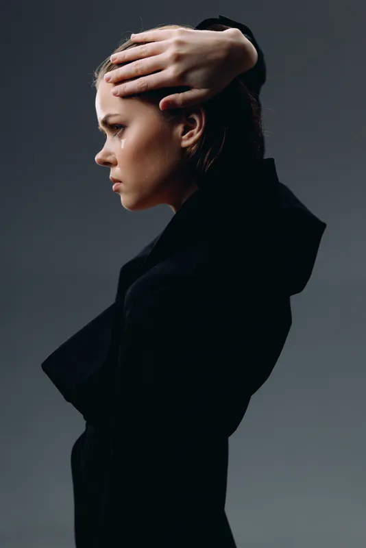 serious woman in black outfit with hand on head, profile portrait with dark gray background