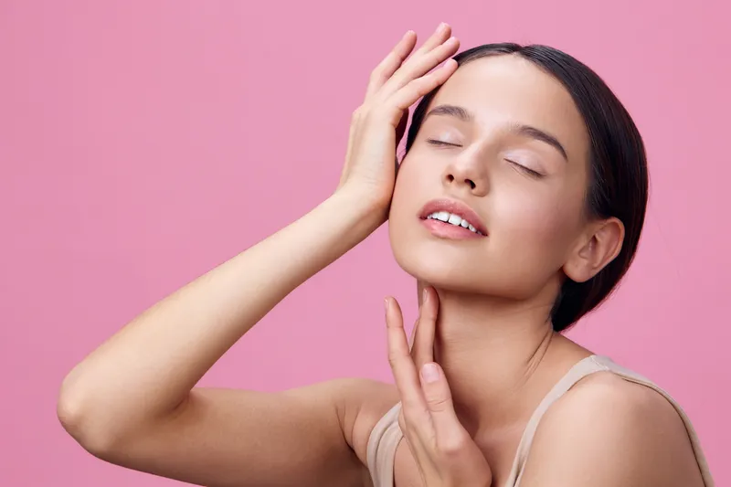 Beautiful young model with glowing skin, posing against a pink background, conveying serenity and confidence, ideal for beauty and skincare concepts