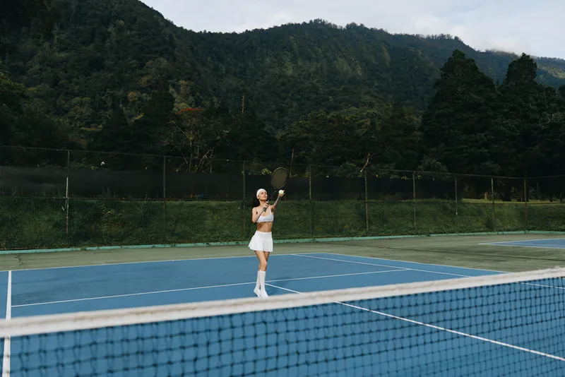 Athletic young female tennis player practicing on a vibrant blue court surrounded by lush green mountains, showcasing determination and focus