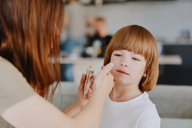 Caring woman applying makeup on a young girl's face, showcasing a warm and loving moment filled with creativity and family bonding in a cozy setting.