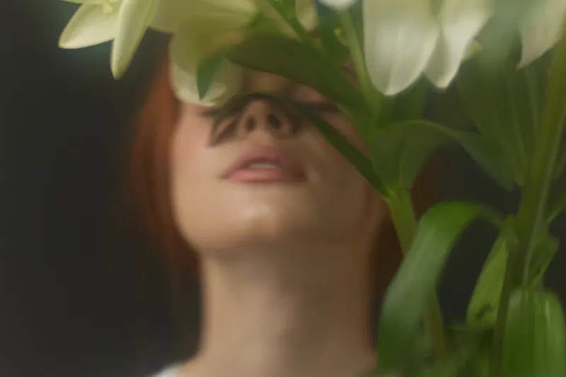 Young woman with red hair interacting with white lilies, showcasing tranquility and elegance in a soft focused composition, ideal for wellness and floral aesthetics