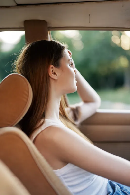 Young woman enjoying a peaceful moment in a car, gazing out the window with a relaxed expression, capturing feelings of freedom and tranquility.