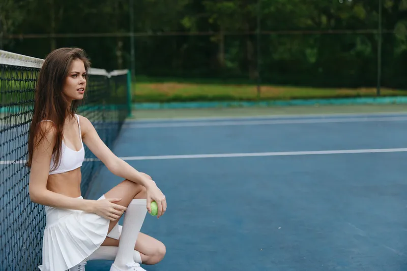 Athletic young woman in sportswear resting on tennis court, showcasing a focused expression and vibrant surroundings Tennis, sport, fitness, youth, health, leisure