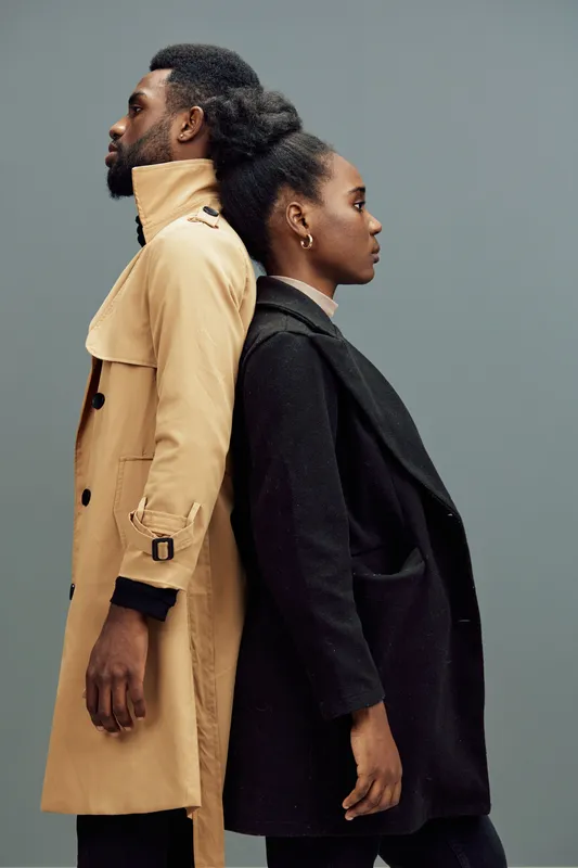Elegant couple in stylish outerwear posing back to back against a neutral backdrop, showcasing contemporary fashion and confidence